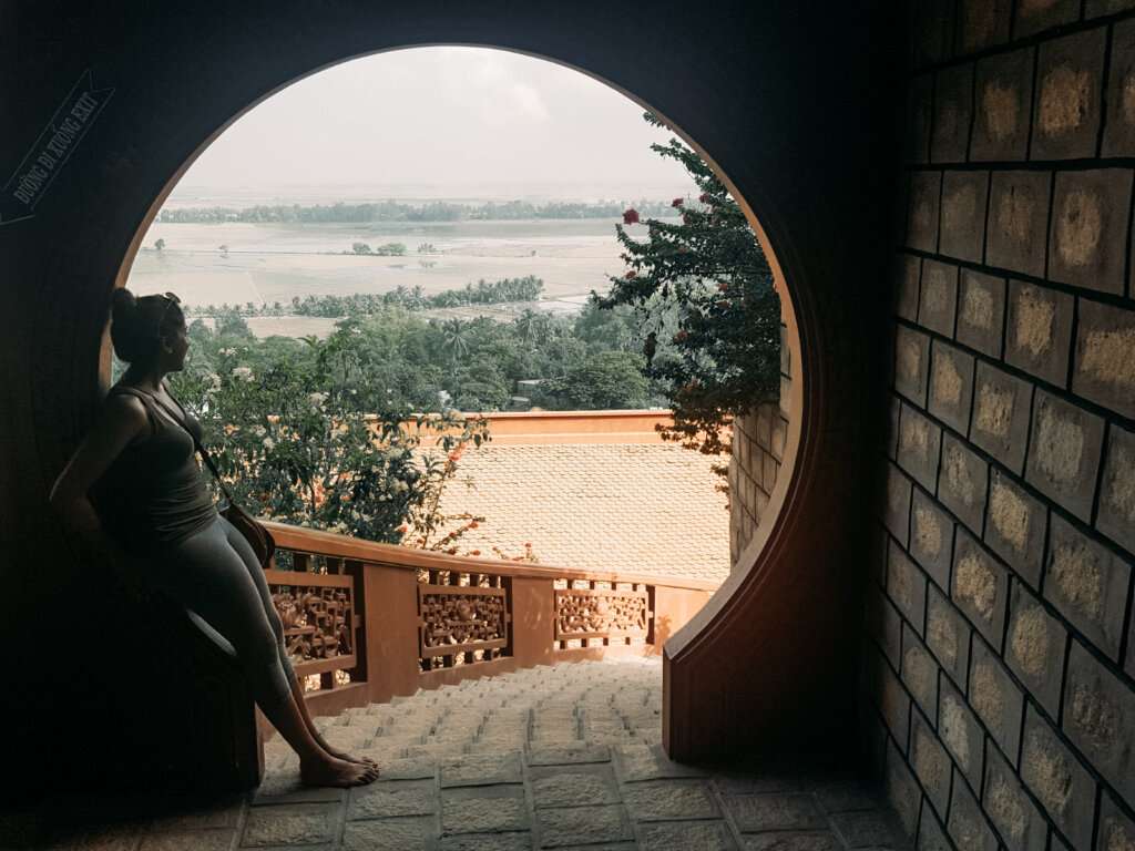 a woman standing in a wide open circle door looking towards the sky and waters