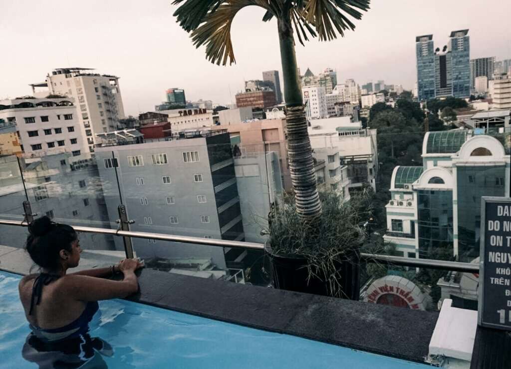 a South Asian woman sitting a pool overlooking a city with a palm tree stretching above her, having found solo travel 