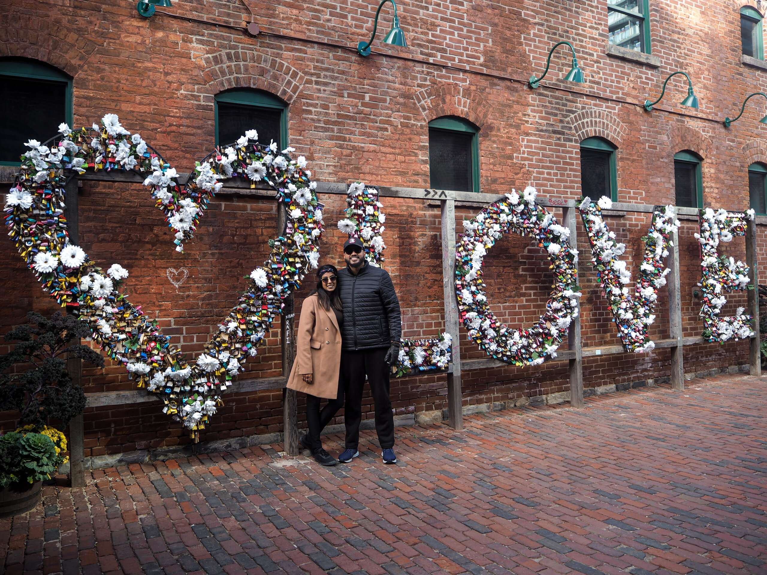 a heart and the word love spelled out with locks, behind a couple wearing a beige and black coat in the distillery district 