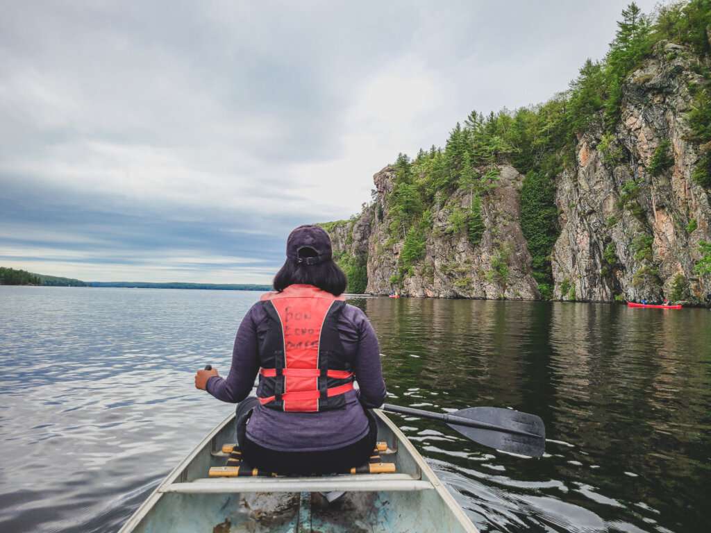 a woman sitting in a canoe with a paddle looking towards a cliff