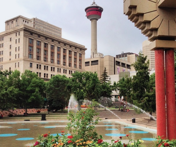 outdoor plaza with water sprinklers, surrounded by flowers, stairs, buildings and and a tall dome tower