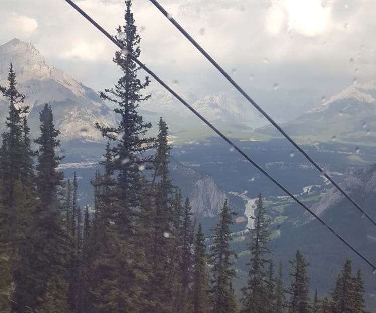 High cable car view of forests in-front of a mountain range with rivers flowing in between the mountains.