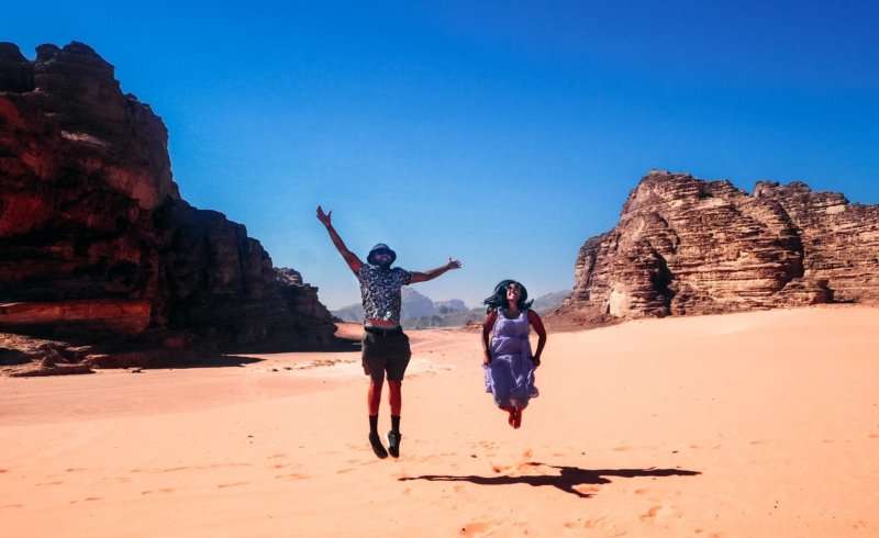 girl and boy jumping in the air with feet of the ground at the desert