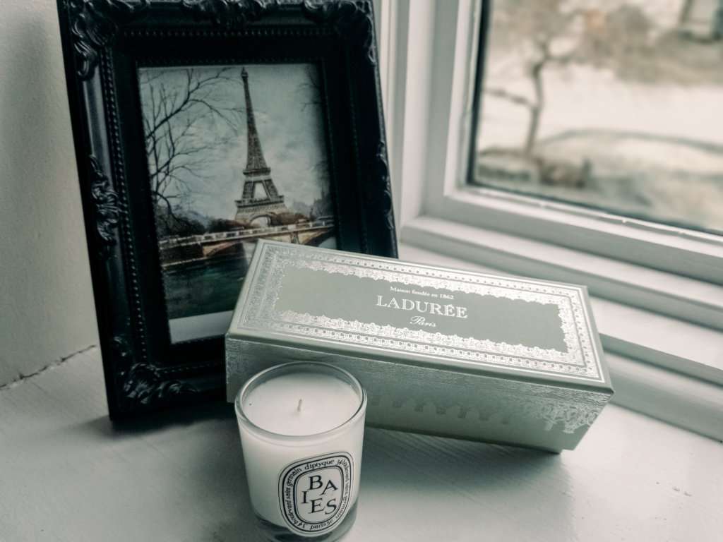 a black picture frame with a picture of the Eiffel Tower in it next to a pale green box with a white candle, all on a window sill in a home