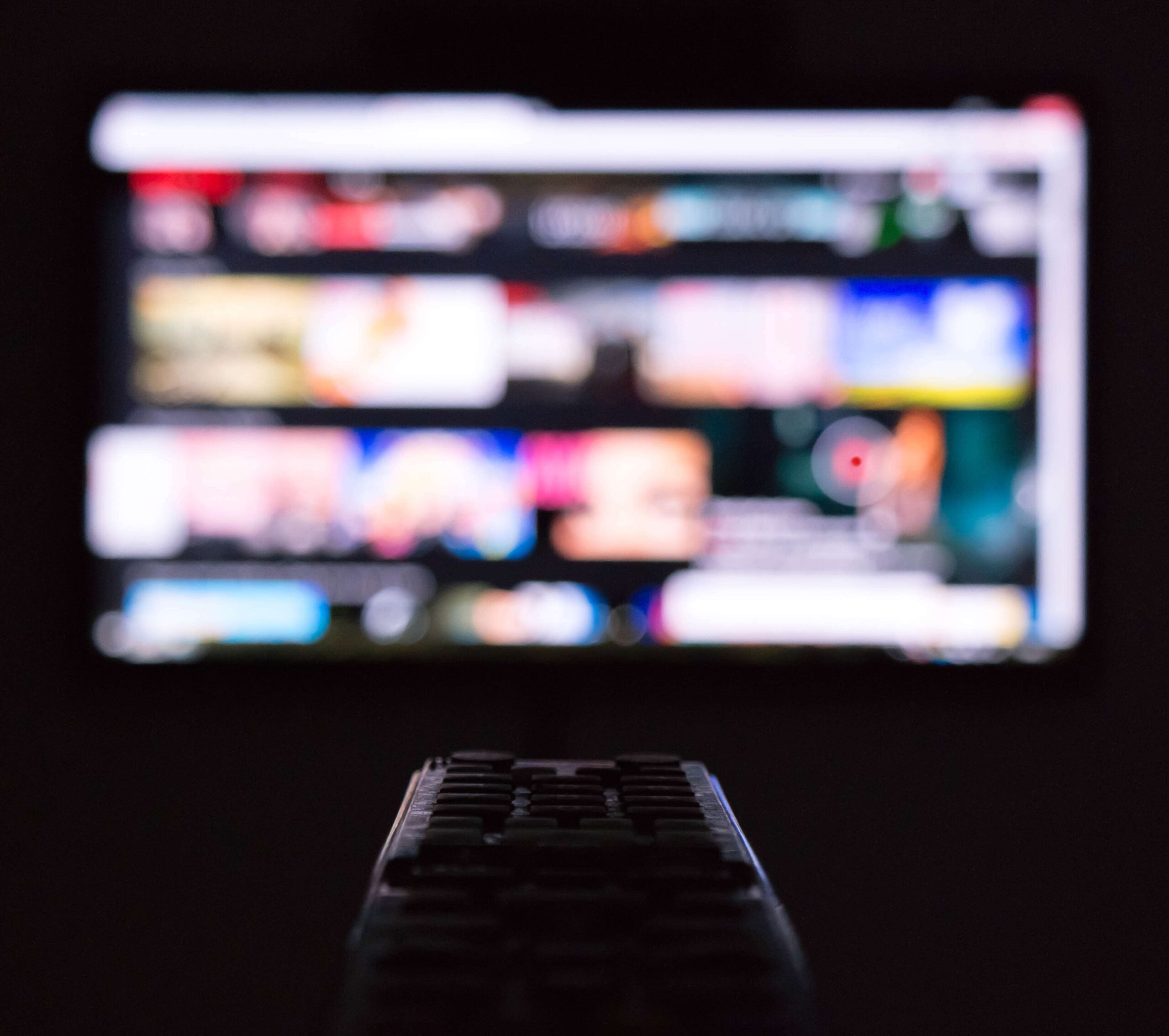 a colorful blurred TV screen with a black remote control facing the tv