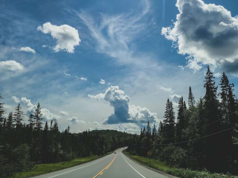 bright blue skies with clouds above a road with greenery on the sides
