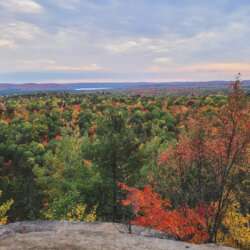 Algonquin Provincial Park with bright colors of red, orange and yellow trees of a forest with a small pond in between from a cliff top view with the blue sky above