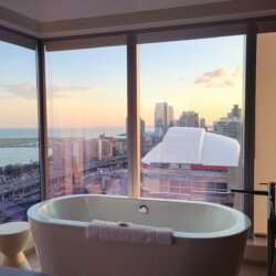 a bathroom with a standing tub against large windows overlooking a city with during the day