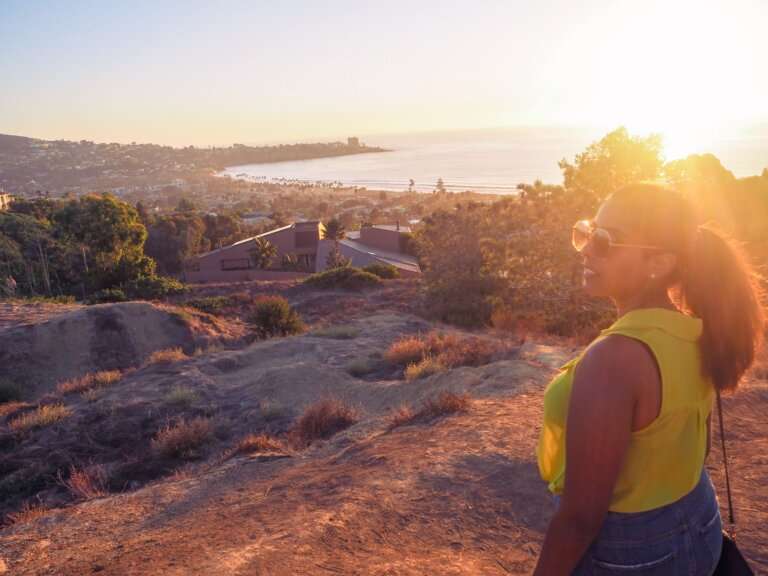 a woman looking to the side standing uphill across a body of water with the sunsetting and thinking about finding ikigai