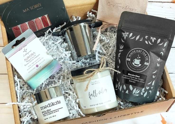 an open subscription box with a black tea bag, candle, white container and a few other items. 