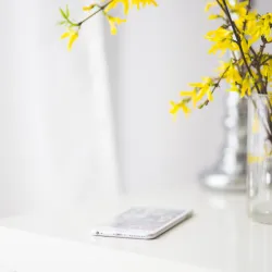 a phone on a white table next to a vase with yellow flowers in it to signify phone affirmation wallpaper