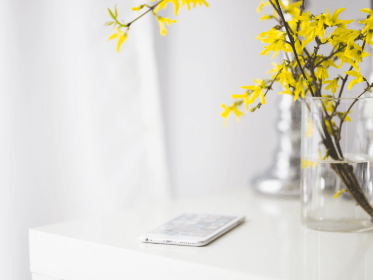a phone on a white table next to a vase with yellow flowers in it to signify phone affirmation wallpaper