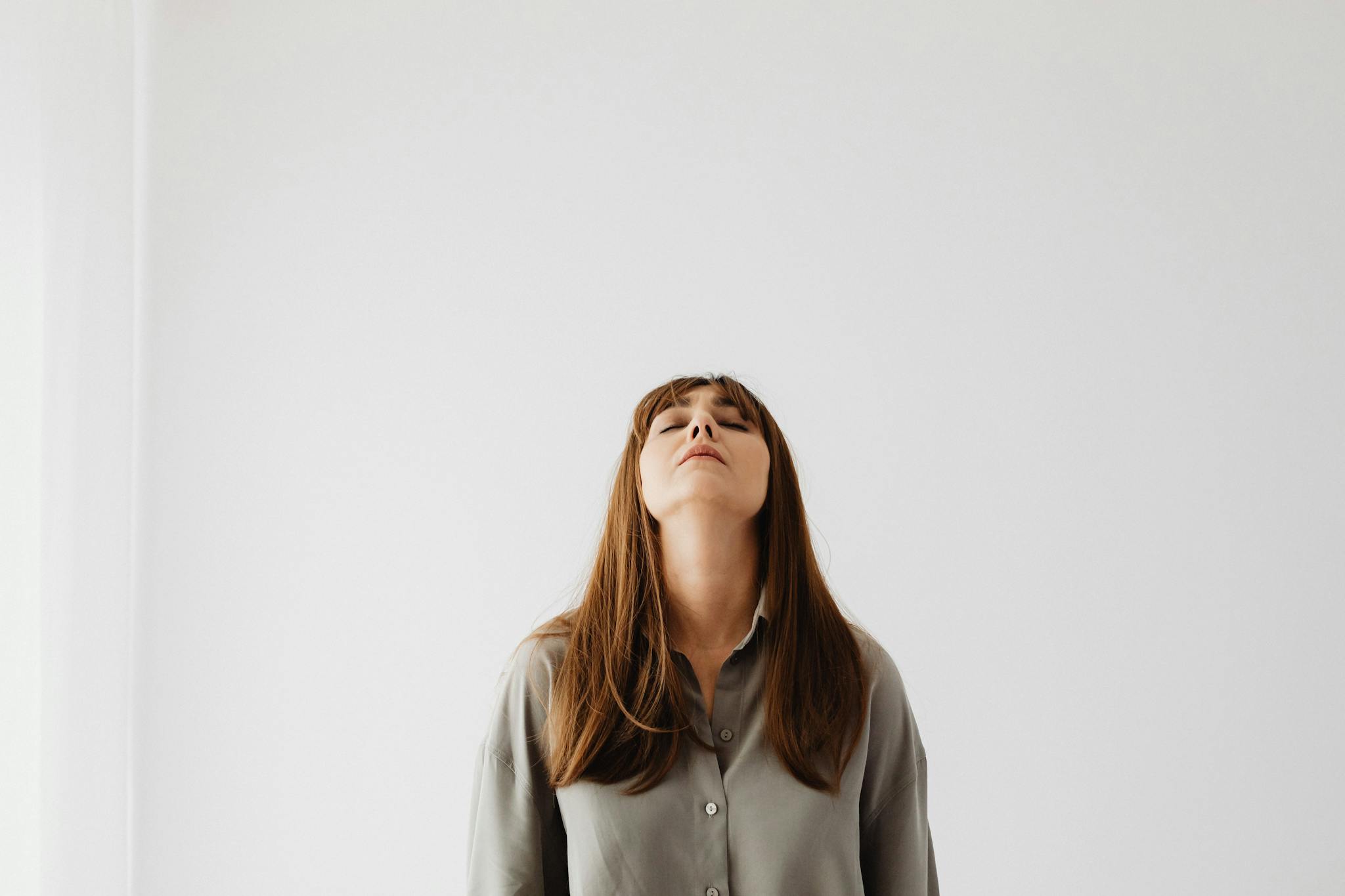 Calm woman with eyes closed, standing still against a white background, conveying tranquility.